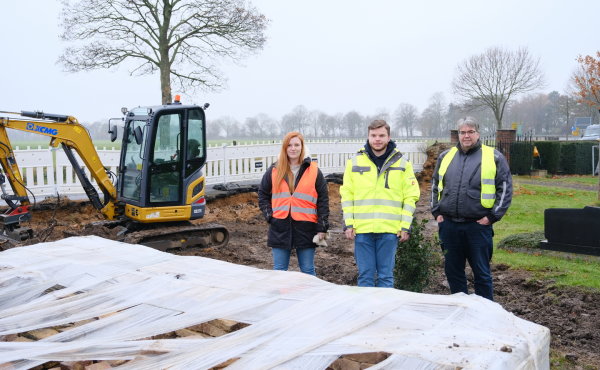 Eva Büchlein (Stabsstelle Wiederaufbau), Philipp Rudolph und Jörg Timmermann (Planungsbüro Schumacher/pbs) stehen vor der zerstörten Friedhofsmauer. Vor ihnen befinden sich die Steine der alten Mauer; im Hintergrund sind ein Bagger und die vorbeiführende B56 zu sehen.